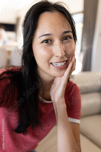 On video call, smiling woman in casual red shirt, relaxing, at home