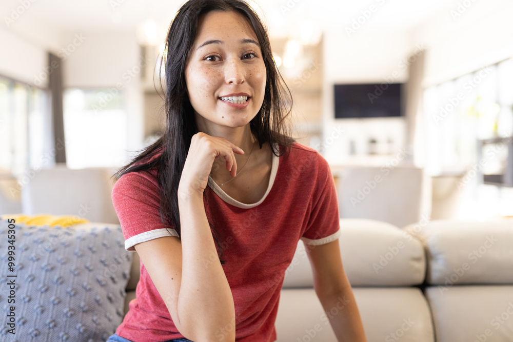 On video call, smiling woman in red shirt sitting on couch, at home On video call, smiling woman in red shirt sitting on couch, at home