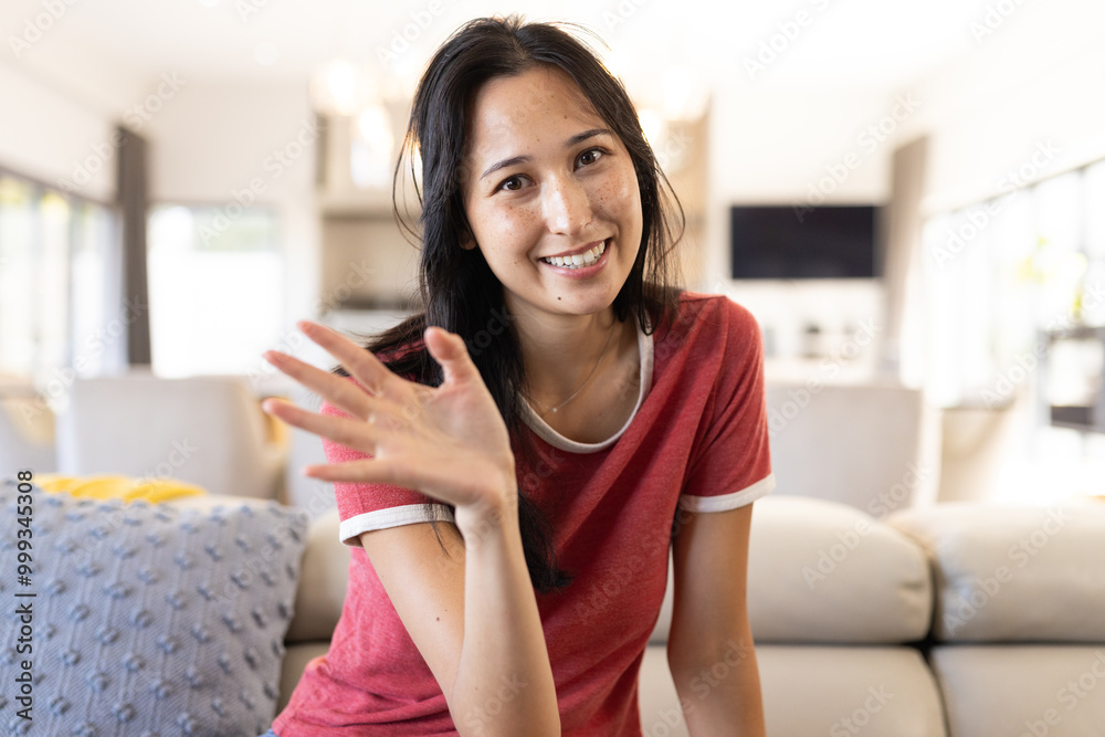 On video call, Smiling woman waving hand while relaxing on couch in cozy living room, at home On video call, Smiling woman waving hand while relaxing on couch in cozy living room, at home
