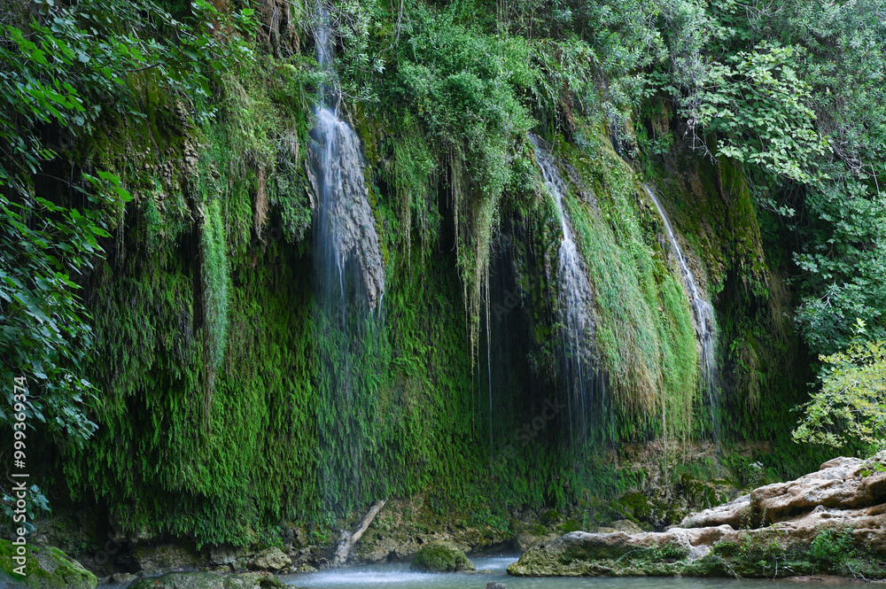 Fototapeta premium A waterfall trickles down the overgrown rocky slopes of a mountain