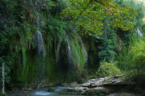 A waterfall trickles down the overgrown rocky slopes of a mountain photo