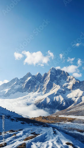 Vertical view of snow-covered mountain peaks with a clear blue sky and scattered clouds, highlighting the rugged terrain.