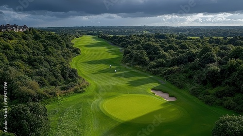 Aerial view of a lush green golf course surrounded by trees under a dramatic cloudy sky.