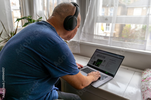 A senior man at home with a wireless headphone and a laptop computer, learning and try to keep up to date with modern technology. A technology use concept.