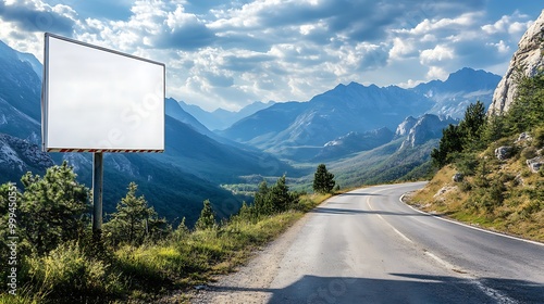 A white billboard placed alongside a winding mountain road, with breathtaking views of rugged peaks and valleys in the distance. photo