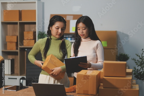 Startup SME small business entrepreneur of freelance Asian woman wearing apron using laptop and box to receive and review orders online to prepare to pack sell to customers, online sme business ideas.