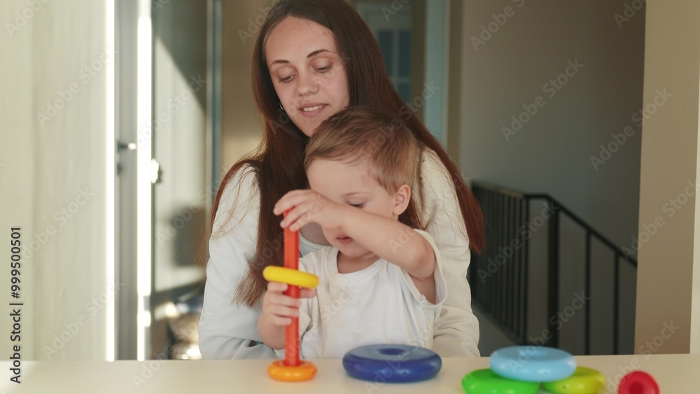 the child collects a toy pyramid. mom plays with son at home happy family. development of fine motor skills in a newborn child. happy family mom and baby play pyramid game. preschool education fun the child collects a toy pyramid. mom plays with son at home happy family. development of fine motor skills in a newborn child. happy family mom and baby play pyramid game. preschool education fun