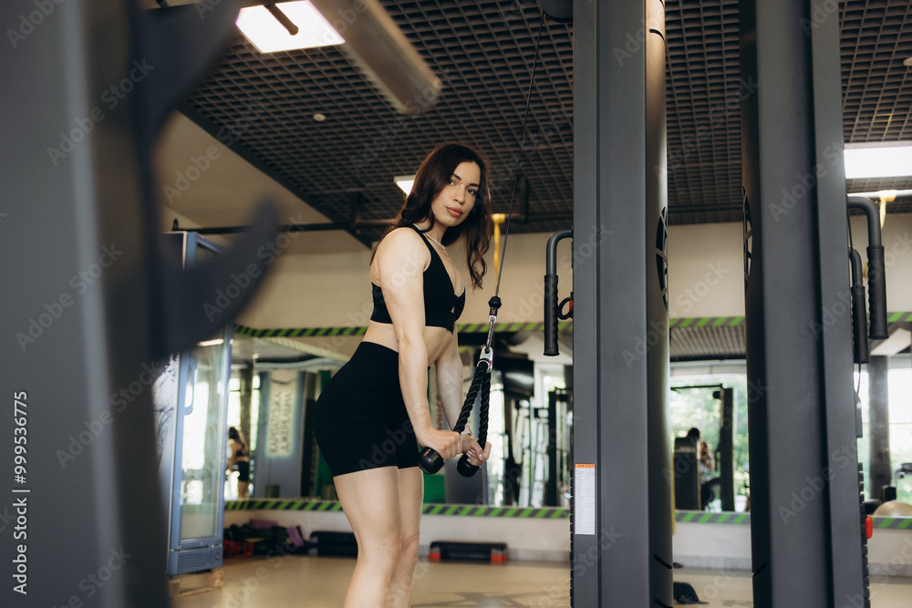 Obraz premium fitness woman doing triceps exercises in the crossover in the gym. Fitness girl in white sport wear with perfect body in gym exercising
