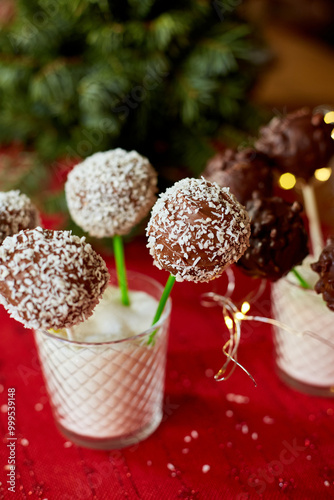 Chocolate cake pops with coconut shavings are displayed in a glass at a celebration, surrounded by festive decorations.