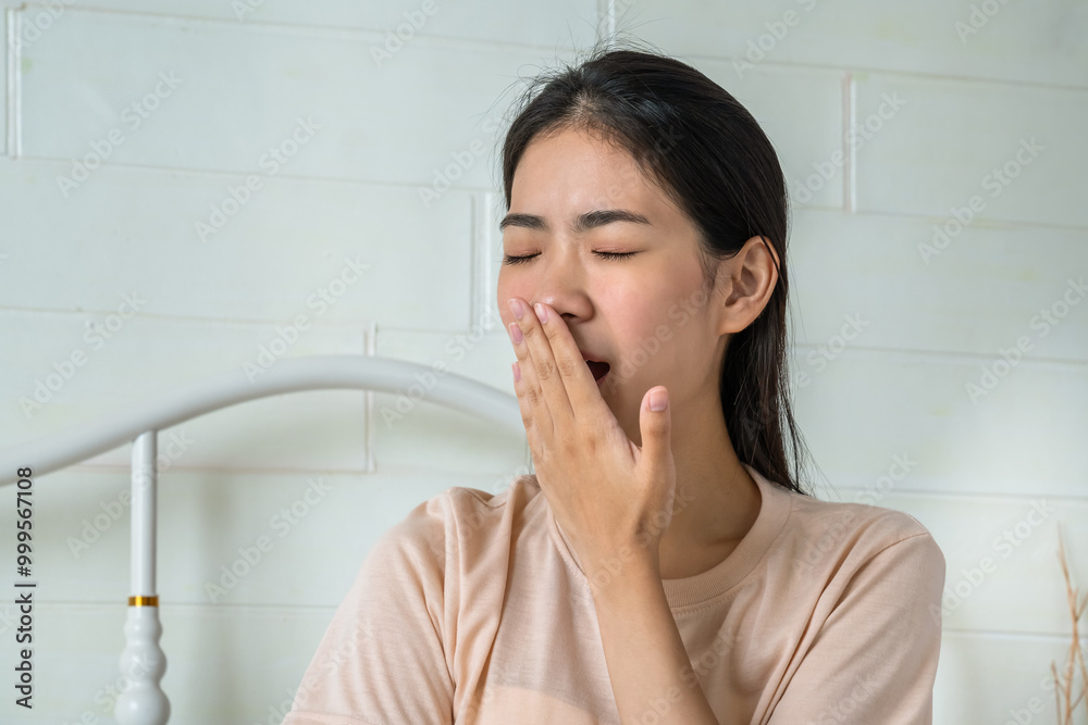 Tired young Asian woman yawning in bed, expressing early morning fatigue Tired young Asian woman yawning in bed, expressing early morning fatigue
