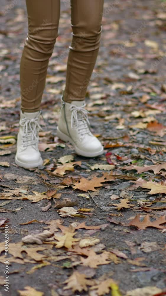Unrecognized lady in beige pants and white jacket and boots walking in the park. Long-haired brunette turning around demonstrating her look. Unrecognized lady in beige pants and white jacket and boots walking in the park. Long-haired brunette turning around demonstrating her look.