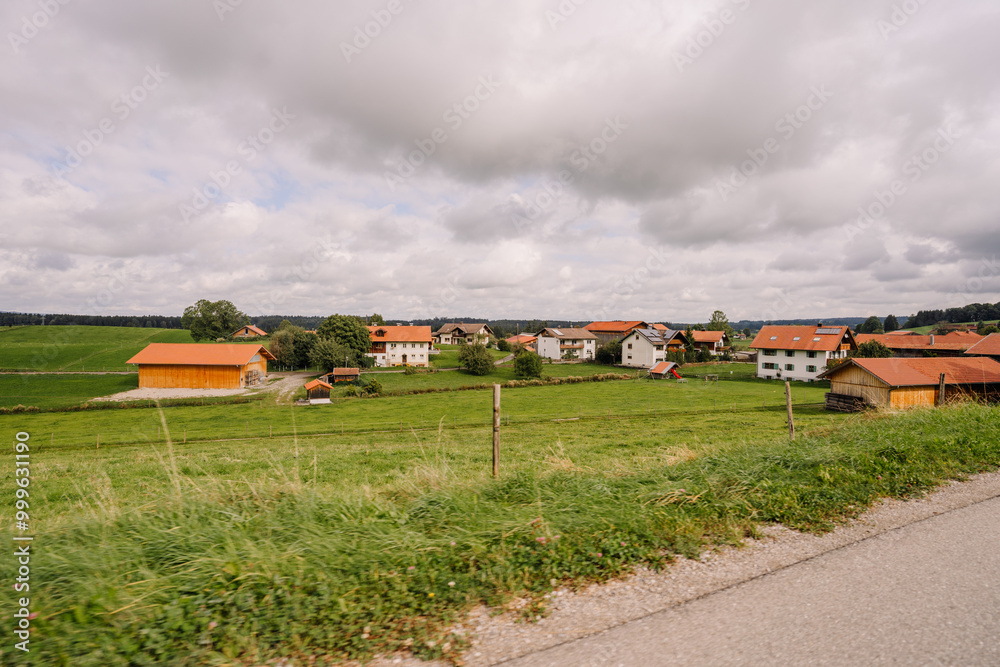 A peaceful rural village in Bavaria with red-roofed houses, green fields, and barns under a cloudy sky, surrounded by lush countryside.. A peaceful rural village in Bavaria with red-roofed houses, green fields, and barns under a cloudy sky, surrounded by lush countryside..