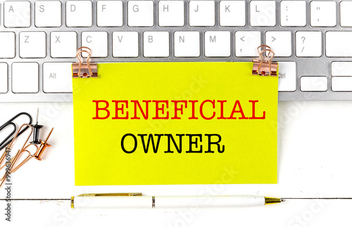 Business concept with beneficial owner message on yellow paper, keyboard, and office supplies on desk