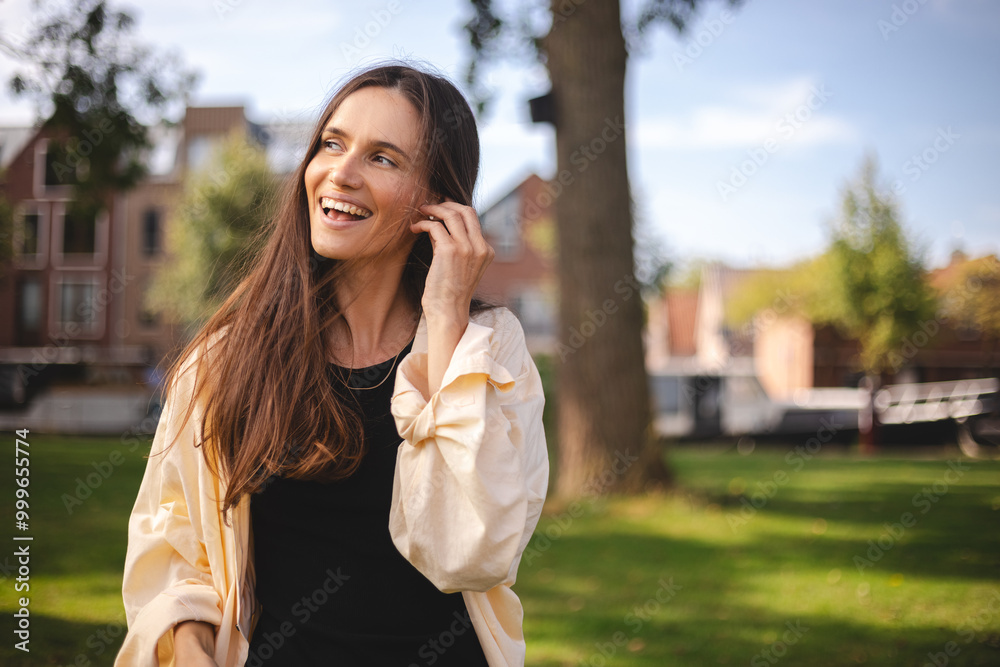 Relaxed young woman brunette in wireless headphones walk on the street listening to music. Enjoying listening to lounge music live via smartphone app, relaxed, look at side, laughing, touch earphones. Relaxed young woman brunette in wireless headphones walk on the street listening to music. Enjoying listening to lounge music live via smartphone app, relaxed, look at side, laughing, touch earphones.