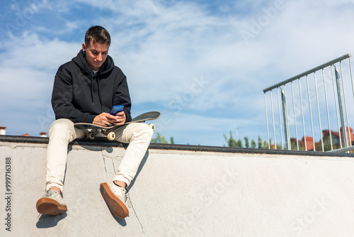 Tableau sur toile copyspace Relaxed skater texting on smartphone while sitting at half-pipe edge d