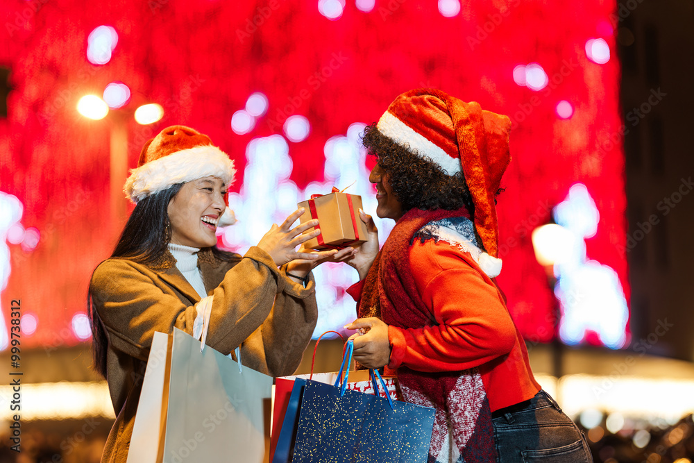 Obraz premium Two happy women exchanging christmas gifts outdoors at night