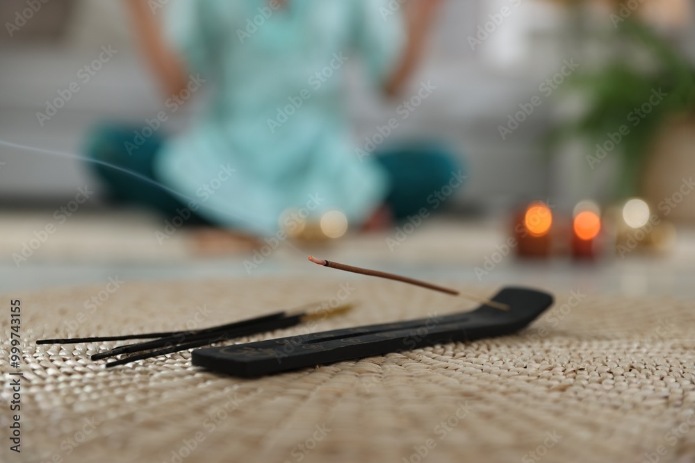 Incense stick smoldering in holder on rug indoors, selective focus Incense stick smoldering in holder on rug indoors, selective focus