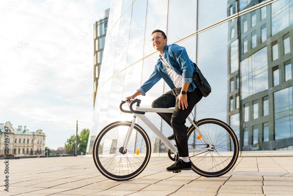 A Young Man Rides a Bicycle Near Modern Architecture on a Sunny Day in an Urban Environment A Young Man Rides a Bicycle Near Modern Architecture on a Sunny Day in an Urban Environment