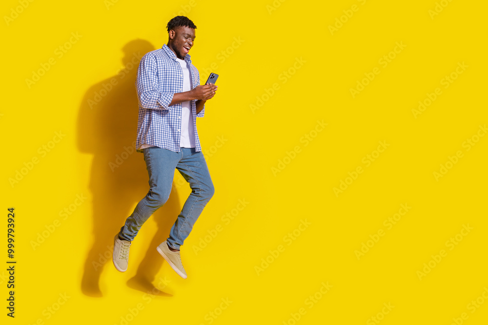 Full length photo of funky cool guy dressed checkered shirt communicating modern device emtpy space isolated yellow color background Full length photo of funky cool guy dressed checkered shirt communicating modern device emtpy space isolated yellow color background