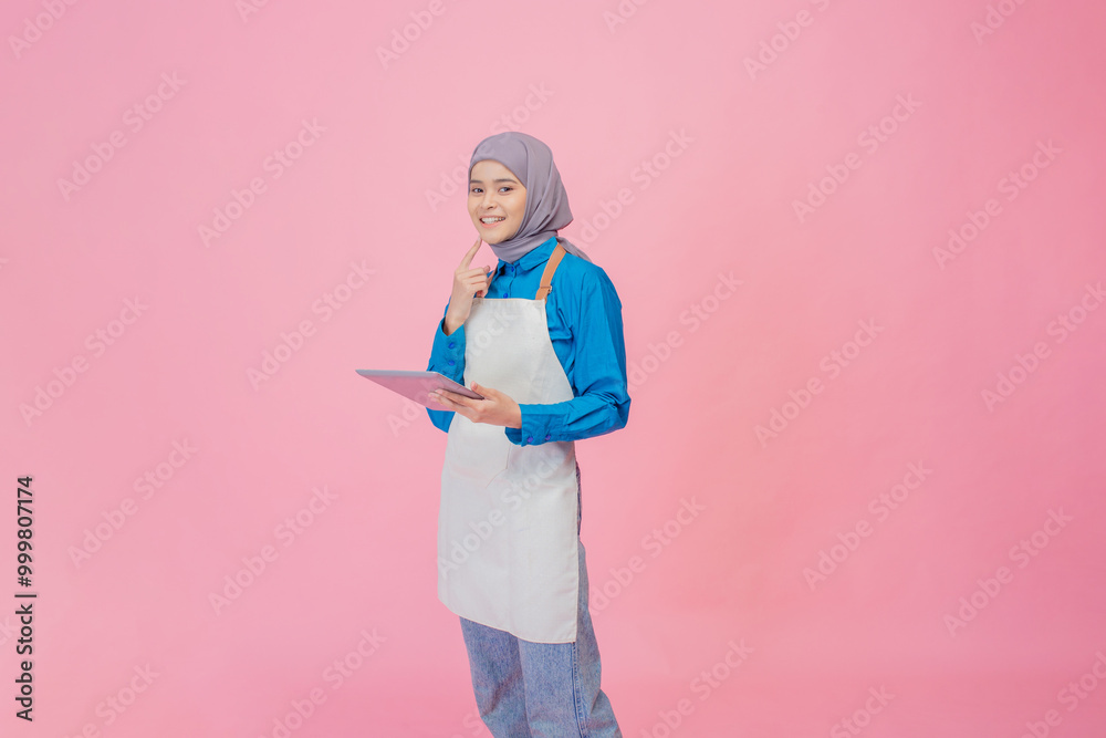A woman in an apron brainstorms with a tablet, set against a creativityenhancing pink backdrop A woman in an apron brainstorms with a tablet, set against a creativityenhancing pink backdrop