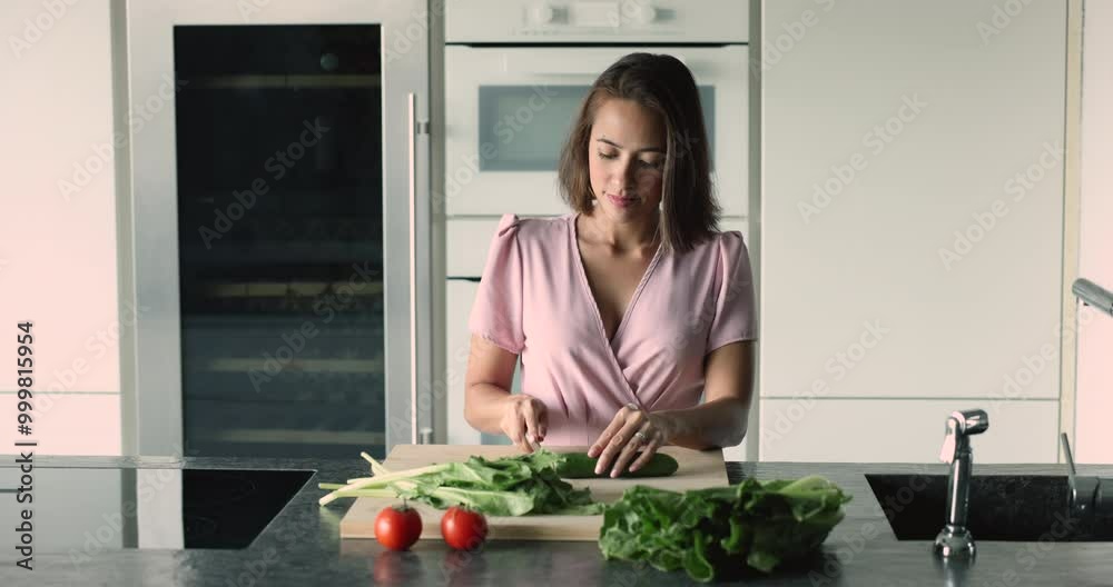 Serious beautiful young Asian girl preparing organic meal from natural ingredients for dinner, slicing fresh cucumber for salad, chopping green vegetables on board, caring for healthy eating Serious beautiful young Asian girl preparing organic meal from natural ingredients for dinner, slicing fresh cucumber for salad, chopping green vegetables on board, caring for healthy eating