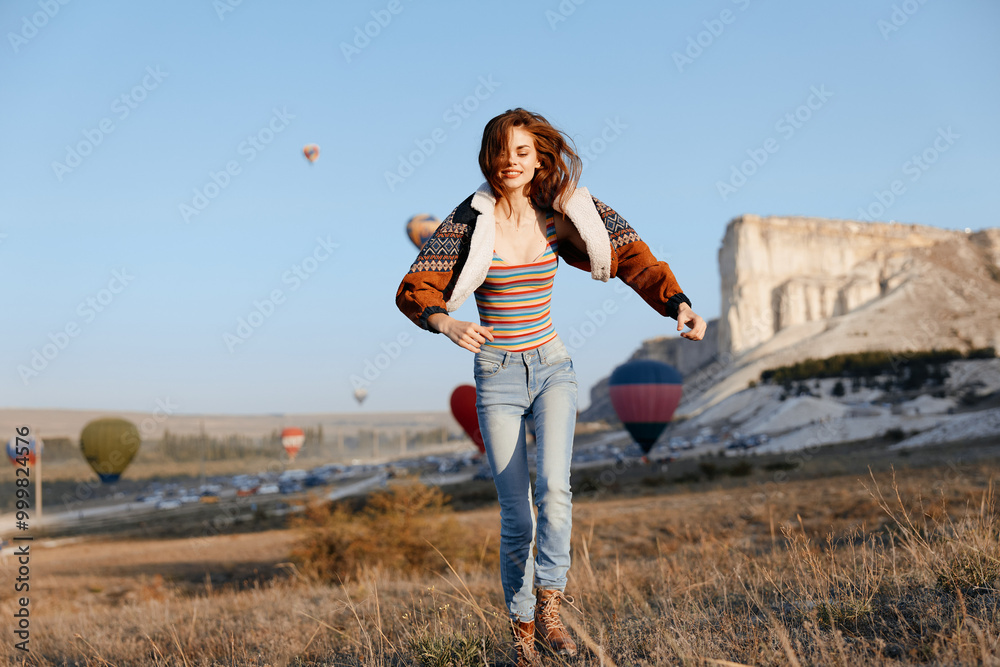 Excited woman leaps with joy as colorful hot air balloons float in the sky behind her Excited woman leaps with joy as colorful hot air balloons float in the sky behind her