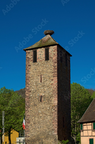 Ancient stone tower with a large stork's nest on the top. Typical architecture of Alsace region. Riquewihr village is a commune in the Haut-Rhin department in Grand Est in north-eastern France