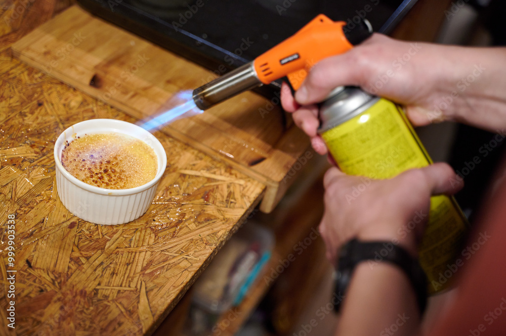 Chef Using a Kitchen Torch to Caramelize Crème Brûlée, Captured Indoors with Warm Ambient Light During a Culinary Demonstration