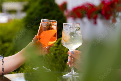 Two women sitting outdoors making a celebratory toast with a an orange spritz and a hugo spritz cocktail