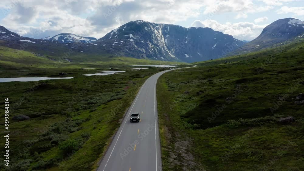 Aerial view of Norway picturesque road with cars, waving through valleys with stunning views of mountains and fjord waterways. Road travel in natural landscapes concept. Drone zoom in footage Aerial view of Norway picturesque road with cars, waving through valleys with stunning views of mountains and fjord waterways. Road travel in natural landscapes concept. Drone zoom in footage