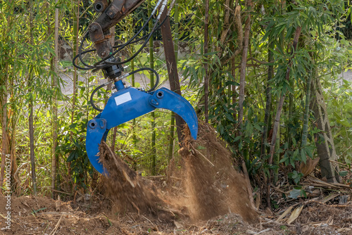 A multifunctional excavator grab with hydraulic rotator moves the soil to clear it of bamboo tree roots
