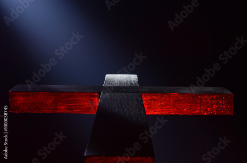 Black wooden Christian cross on a black background illuminated from above