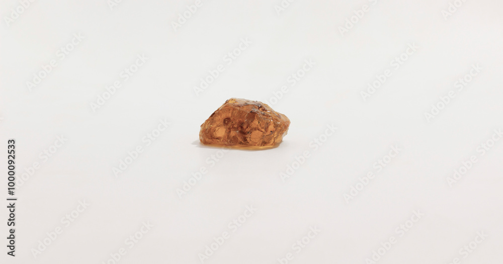 A single small, irregularly shaped amber colored gemstone on smooth, neutral background. A single small, irregularly shaped amber colored gemstone on smooth, neutral background.