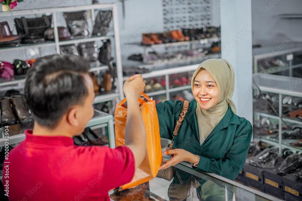 Fototapeta premium high angle view of hijab customer taking purchased product from leather shoes store male staff