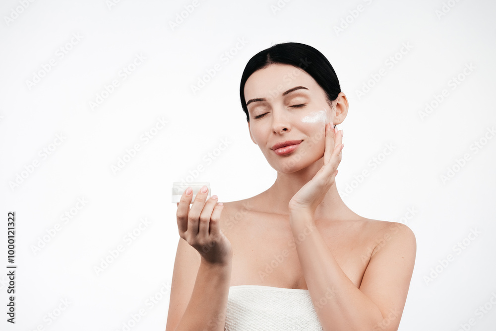 Beauty portrait of brunette woman in white towel, applies cream to the face. Skincare cleansing eco organic cosmetic spa relax concept. Free copy space for text, banner. Cosmetics advertising Beauty portrait of brunette woman in white towel, applies cream to the face. Skincare cleansing eco organic cosmetic spa relax concept. Free copy space for text, banner. Cosmetics advertising