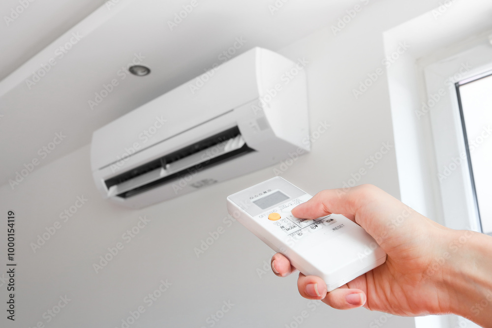 Air conditioner temperature adjustment with remote controller in room at home. Hand holding remote controller of air conditioner inside the white room and set at cool temperature Air conditioner temperature adjustment with remote controller in room at home. Hand holding remote controller of air conditioner inside the white room and set at cool temperature