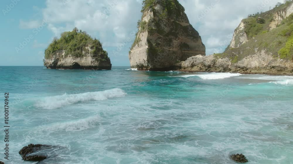 Serene view of towering cliffs with lush greenery surrounded by turquoise waves crashing onto the rocks at Diamond Beach, Nusa Penida. Serene view of towering cliffs with lush greenery surrounded by turquoise waves crashing onto the rocks at Diamond Beach, Nusa Penida.
