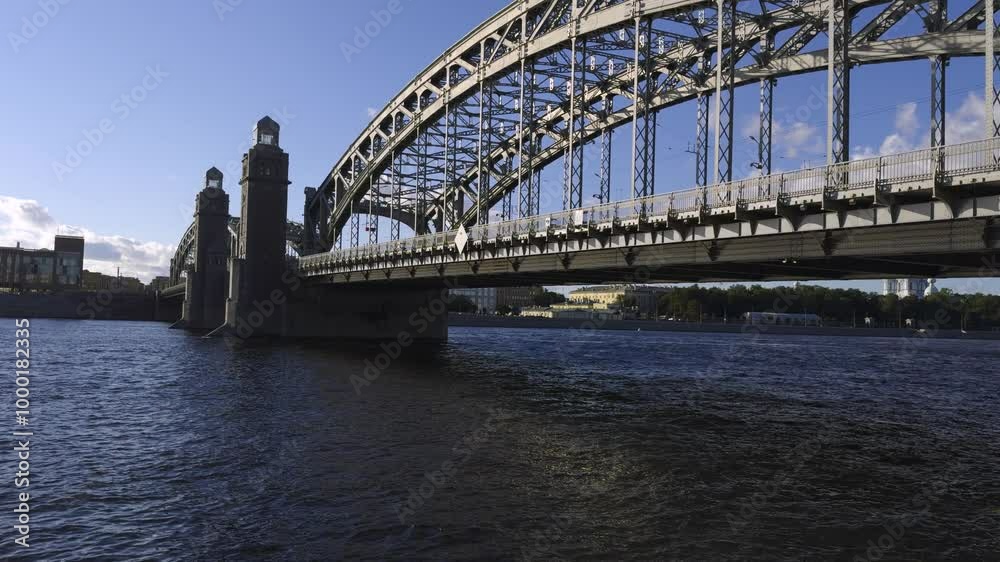 A beautiful wide-angle shot of the iconic Bolshoy Obukhovsky Bridge in Saint Petersburg under a clear blue sky. The image captures the bridge arches, towers, and surrounding water with natural A beautiful wide-angle shot of the iconic Bolshoy Obukhovsky Bridge in Saint Petersburg under a clear blue sky. The image captures the bridge arches, towers, and surrounding water with natural