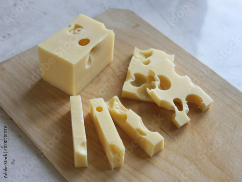 A block of maasdam cheese and sliced pieces on a wooden board on a white background. Dairy products, cheese making. Maasdam and radomer - cheese with big holes photo