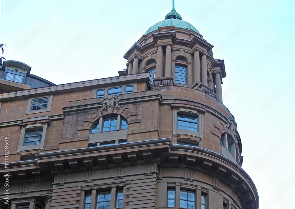Fototapeta premium The top front corner of an old rounded sandstone building. Domed roof with columns and arched windows.