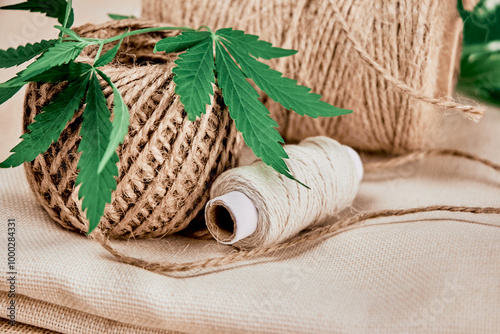 skein, ball and spool of natural hemp fiber threads with green cannabis leaf are on hemp fabric close-up, eco-friendliness and durability of textiles concept
