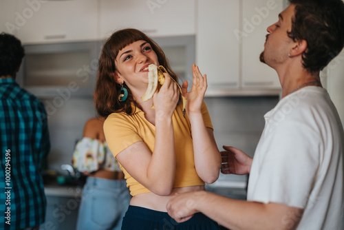 Young adults enjoy a casual social gathering in the kitchen, with one person playfully eating a banana while interacting joyfully with friends. photo