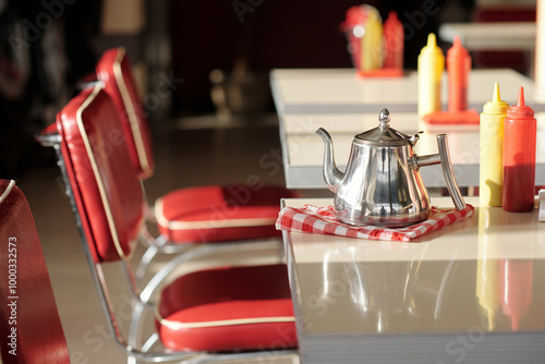 Retro diner setting featuring red chairs and metal coffee pot on checkered napkin surrounded by condiment bottles