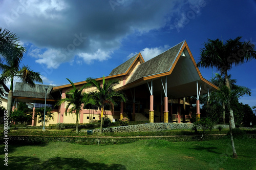A serene villa surrounded by lush greenery, featuring a traditional yet modern architectural design with a sloping red-tiled roof. The villa is nestled amidst a garden landscape