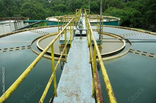 a water treatment facility featuring several large storage tanks filled with water. Surrounding the tanks are large green pipes, likely used to transfer water between the tanks