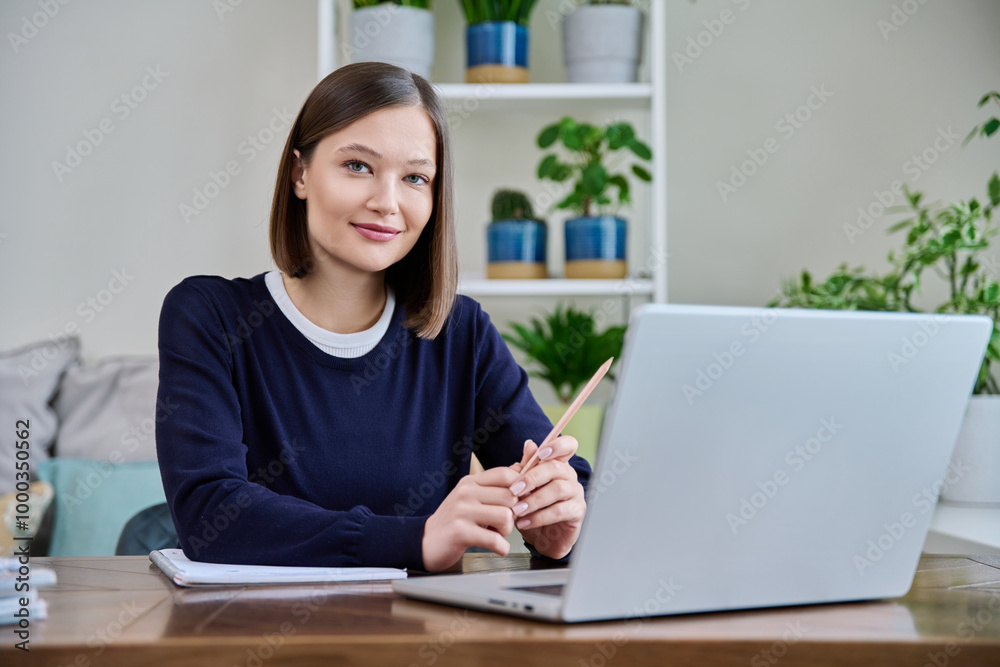 Portrait of young woman at her workplace at desk with laptop, looking at camera Portrait of young woman at her workplace at desk with laptop, looking at camera