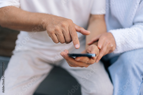 Closeup cropped shot of elderly married couple using smartphone, exploring apps, staying connected with world, embracing digital age in retirement. Senior male and female typing phone together outside