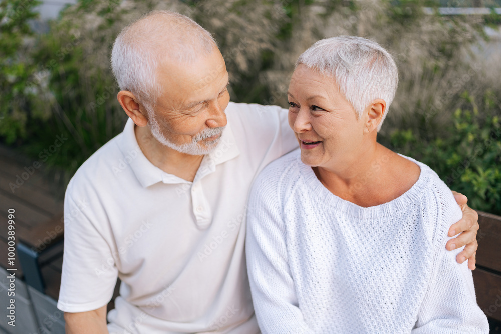 Closeup portrait of charming senior couple enjoying each other company sitting on bench on summer day, loving looking at each other, showcasing beauty of enduring love and companionship. Closeup portrait of charming senior couple enjoying each other company sitting on bench on summer day, loving looking at each other, showcasing beauty of enduring love and companionship.