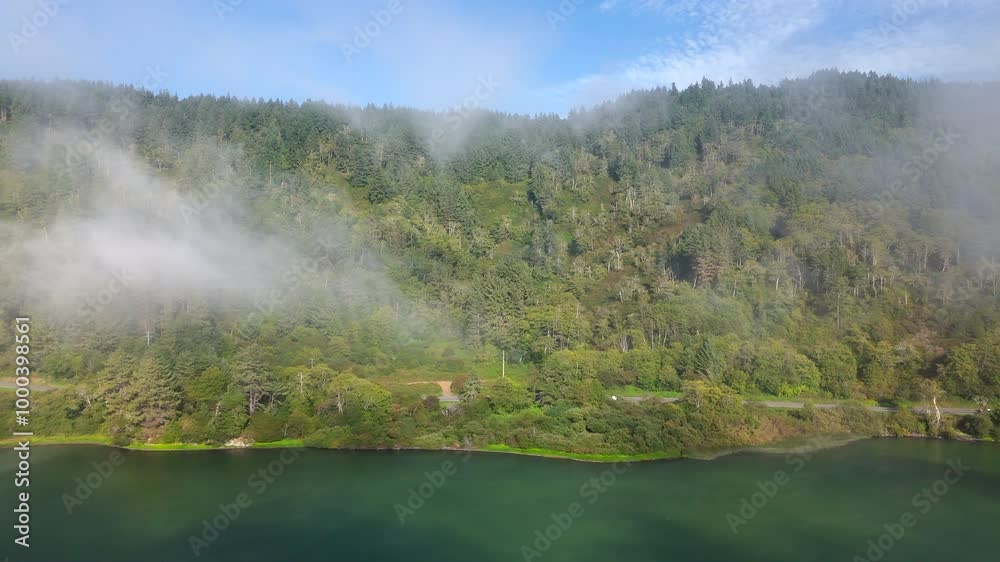 Stunning aerial shot beautifully captures the breathtaking Oregon coast, showcasing its lush green forests beneath the misty, foggy skies that hover gracefully above the tranquil waters below