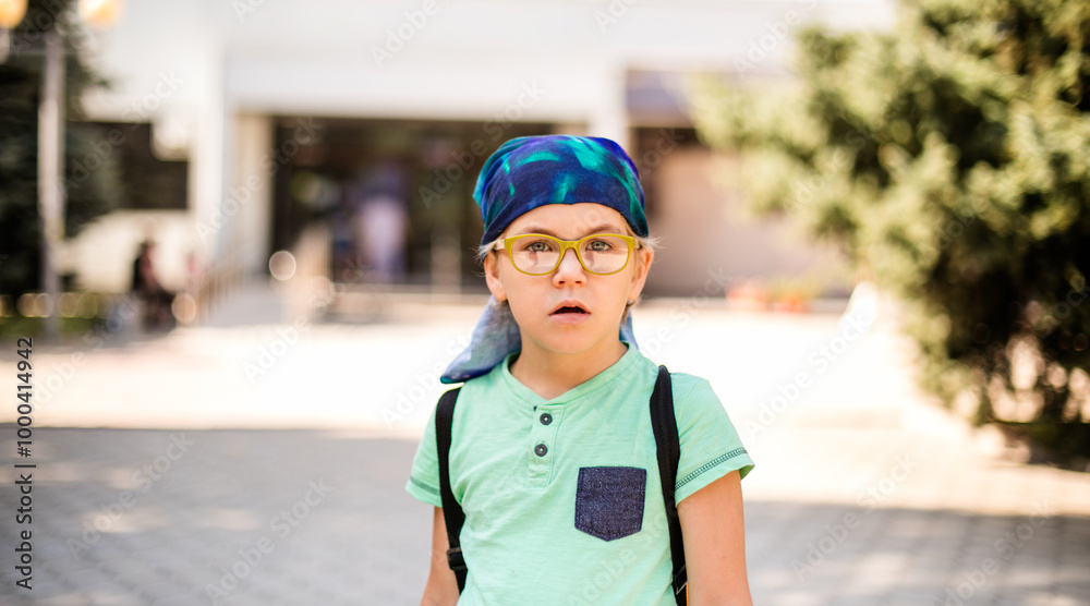 A playful small boy in glasses and a headband, dressed in a green shirt and jean shorts, laughing A playful small boy in glasses and a headband, dressed in a green shirt and jean shorts, laughing